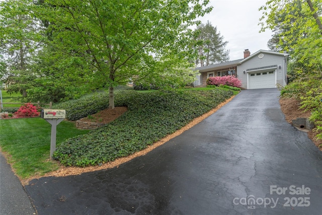 view of front of property with an attached garage, a chimney, driveway, and a front lawn
