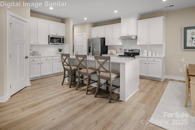 kitchen with visible vents, a kitchen island with sink, light wood-type flooring, light countertops, and stainless steel appliances