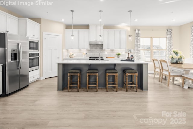 kitchen with a sink, decorative backsplash, light wood finished floors, and stainless steel appliances