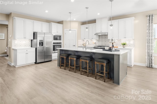 kitchen featuring decorative backsplash, a kitchen bar, appliances with stainless steel finishes, a sink, and under cabinet range hood