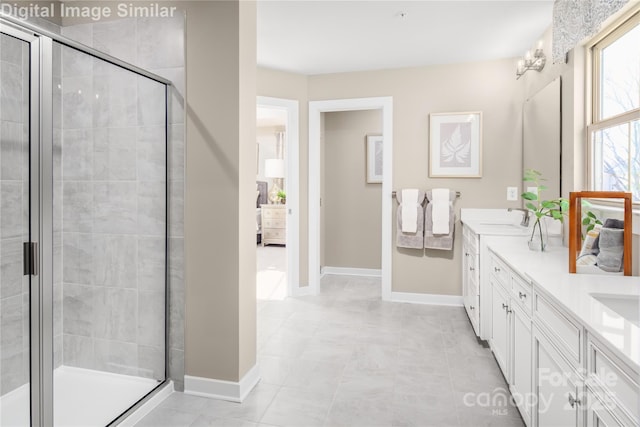 full bathroom with baseboards, double vanity, a sink, and a stall shower