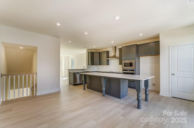 2907 W Trade St, Charlotte, NC 28208 - kitchen with stainless steel appliances, wall chimney exhaust hood, light countertops, a center island, and light wood-style floors