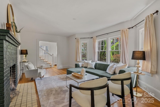 living room featuring stairway, a brick fireplace, baseboards, and light wood-style floors