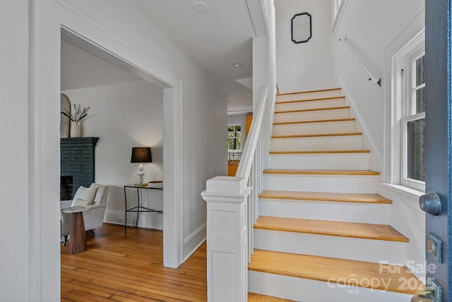 stairs with a brick fireplace, wood-type flooring, and baseboards