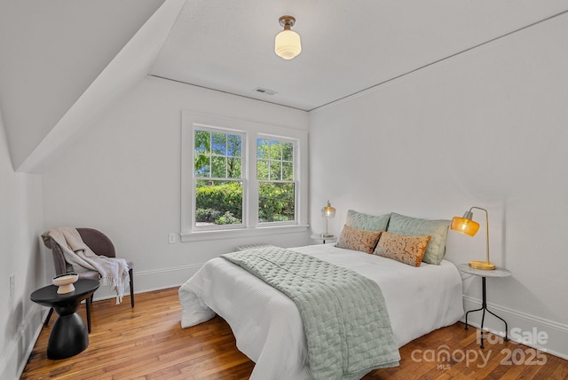bedroom with vaulted ceiling, baseboards, visible vents, and wood finished floors