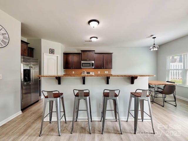 6541 Hasley Woods Dr, Huntersville, NC 28078 - kitchen featuring dark brown cabinetry, baseboards, light wood-style floors, a breakfast bar, and stainless steel appliances