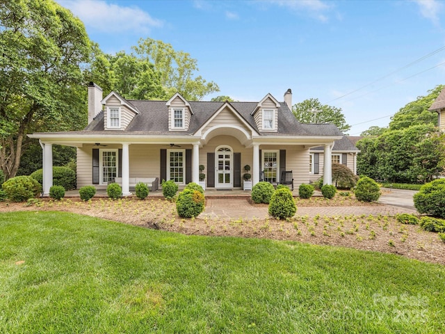 cape cod house featuring a chimney, covered porch, a ceiling fan, and a front lawn