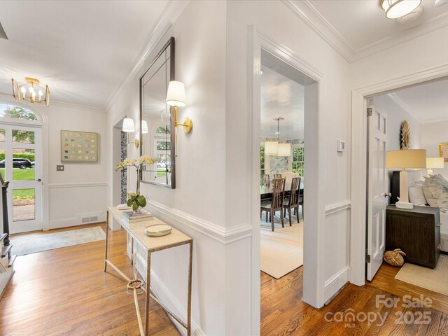 foyer entrance featuring a chandelier, wood finished floors, plenty of natural light, ornamental molding, and baseboards