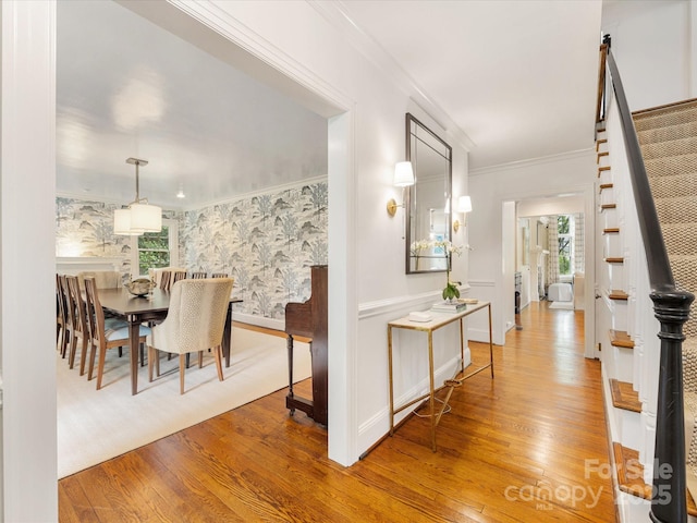 corridor featuring stairway, wood finished floors, healthy amount of natural light, ornamental molding, and wallpapered walls