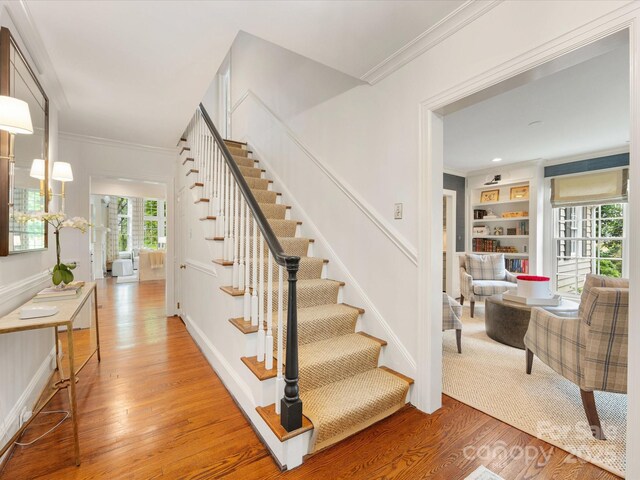 staircase featuring ornamental molding, wood finished floors, built in features, and baseboards