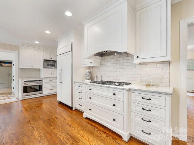 kitchen featuring stainless steel appliances, decorative backsplash, white cabinets, light stone counters, and light wood-style floors