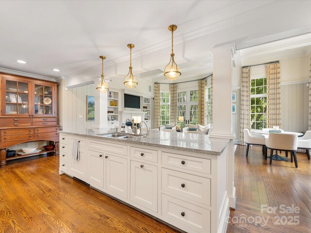 kitchen featuring a sink, open floor plan, decorative columns, crown molding, and light stone counters