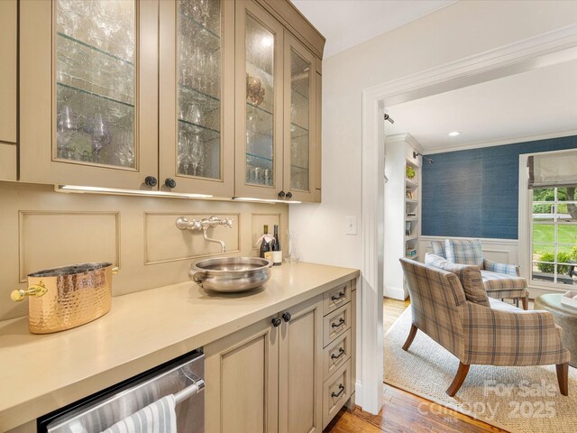 bar area with light wood-style floors, a wainscoted wall, dishwasher, a decorative wall, and crown molding
