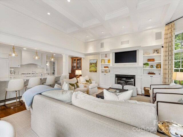 living room with light wood finished floors, beam ceiling, a glass covered fireplace, coffered ceiling, and recessed lighting