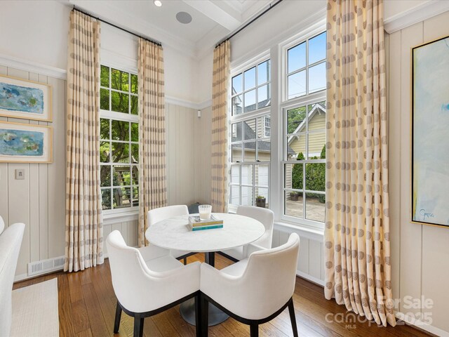 dining area featuring wood-type flooring, ornamental molding, and a decorative wall