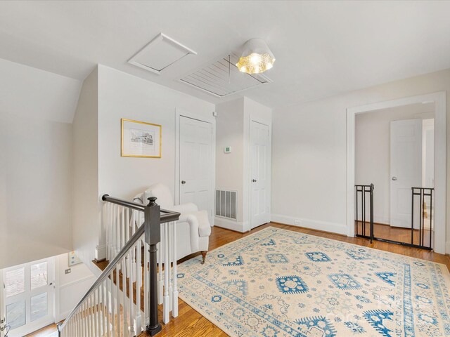 corridor with an upstairs landing, wood finished floors, attic access, and baseboards