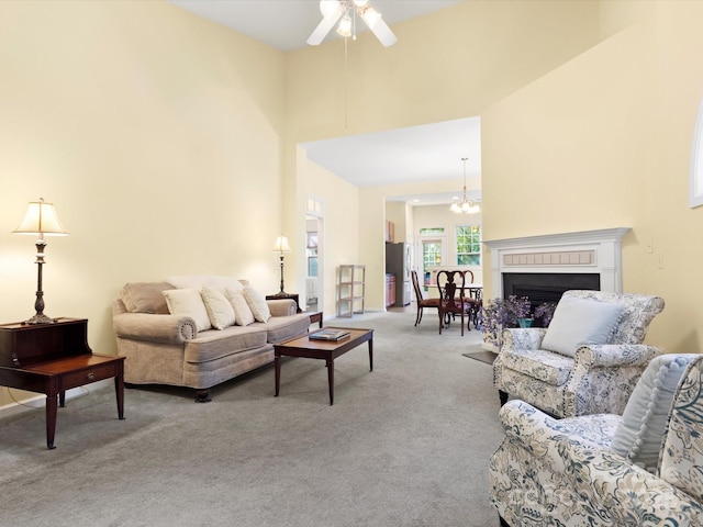 living room featuring a fireplace, a high ceiling, carpet, and ceiling fan with notable chandelier