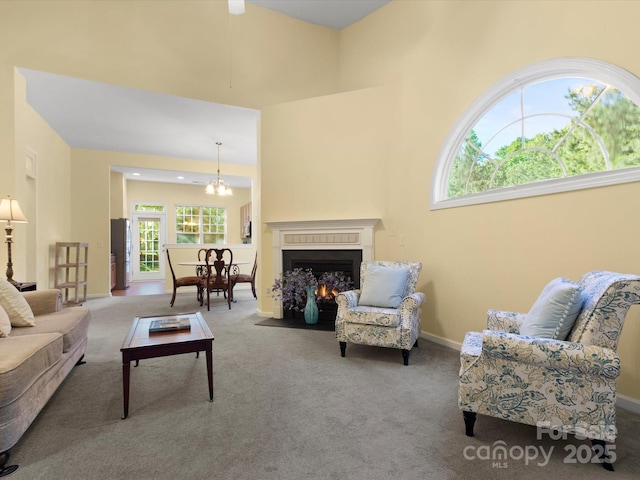 living area featuring carpet flooring, a notable chandelier, a fireplace with flush hearth, and a healthy amount of sunlight