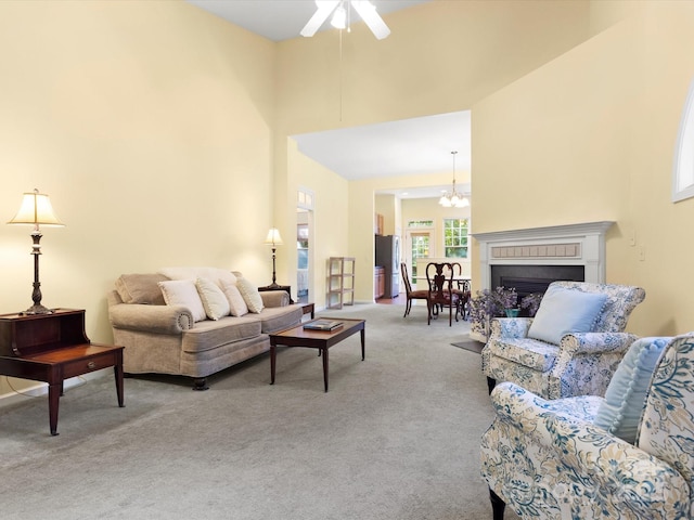 living area with a fireplace, carpet, ceiling fan with notable chandelier, and a towering ceiling