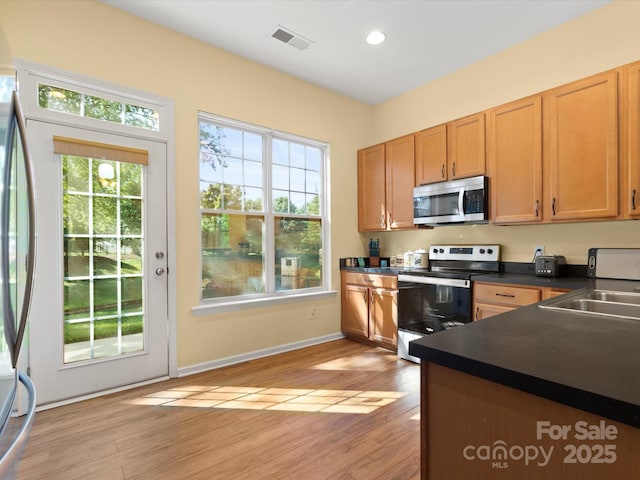 kitchen featuring visible vents, appliances with stainless steel finishes, dark countertops, a sink, and light wood finished floors