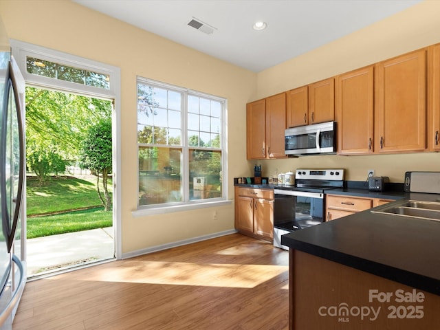 kitchen featuring dark countertops, appliances with stainless steel finishes, a sink, light wood finished floors, and recessed lighting