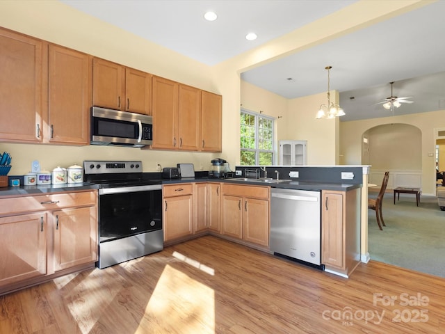 kitchen with dark countertops, appliances with stainless steel finishes, light wood-style floors, and arched walkways