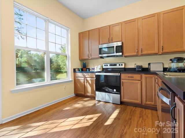 kitchen featuring dark countertops, appliances with stainless steel finishes, light wood-type flooring, a sink, and baseboards