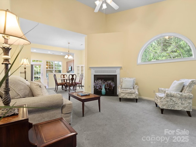 living room featuring carpet floors, a ceiling fan, a fireplace with flush hearth, and plenty of natural light