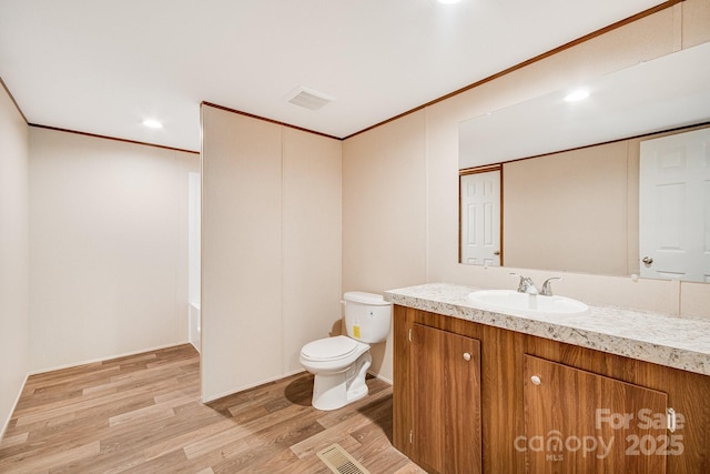 bathroom with toilet, wood finished floors, vanity, crown molding, and a tub