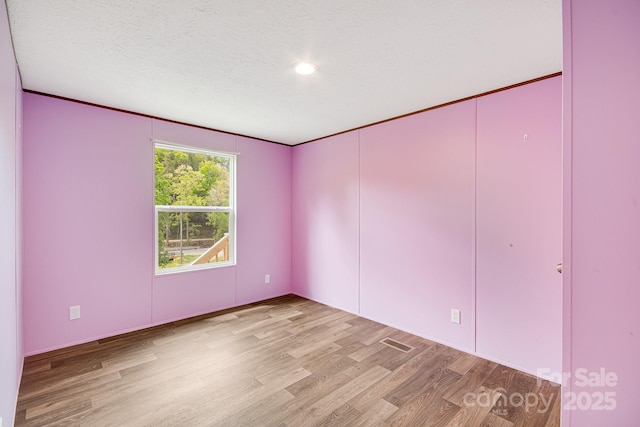 empty room with light wood finished floors and a textured ceiling