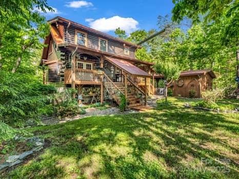 back of house featuring stairway, a deck, log siding, and a lawn