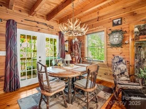 dining space featuring beamed ceiling, wooden walls, wood ceiling, french doors, and a notable chandelier