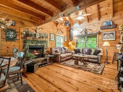 living area featuring ceiling fan, hardwood / wood-style flooring, wooden ceiling, lofted ceiling with beams, and wooden walls