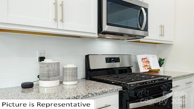 kitchen with gas range oven, stainless steel microwave, white cabinets, tasteful backsplash, and light stone counters