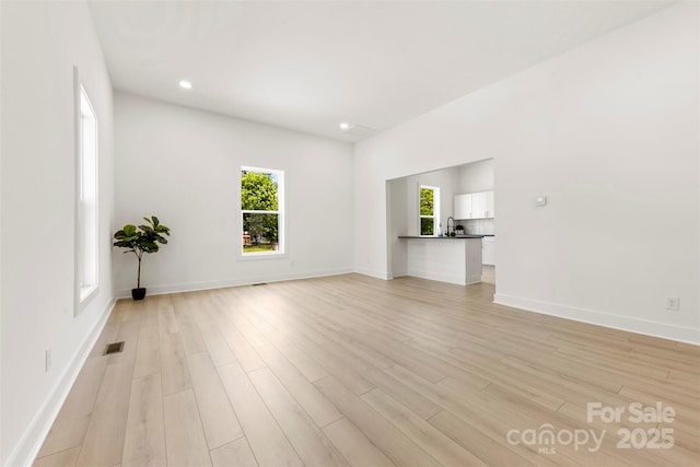 unfurnished living room with baseboards, light wood finished floors, and visible vents