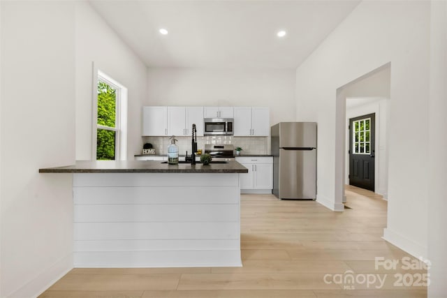 kitchen featuring dark countertops, appliances with stainless steel finishes, a sink, white cabinets, and light wood-style floors
