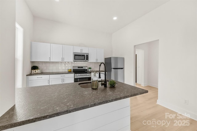 kitchen featuring light wood-type flooring, white cabinetry, a sink, backsplash, and stainless steel appliances