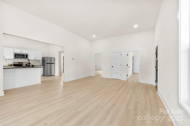 unfurnished living room featuring light wood-style floors, baseboards, recessed lighting, and a sink