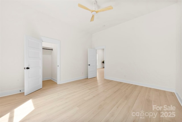 unfurnished bedroom with a walk in closet, baseboards, a ceiling fan, and light wood-style flooring