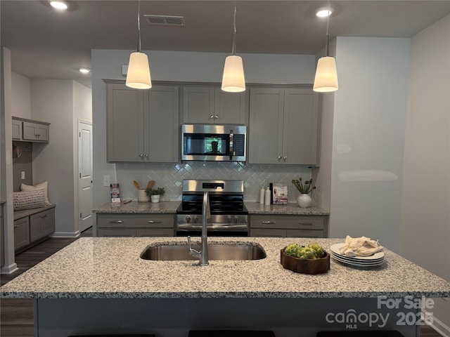 kitchen with a kitchen island with sink, dark wood finished floors, gray cabinets, stainless steel appliances, and decorative backsplash