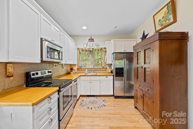 102 Altamahaw Ave, Black Mountain, NC 28711 - kitchen with stainless steel appliances, a sink, white cabinetry, decorative backsplash, and light wood-type flooring