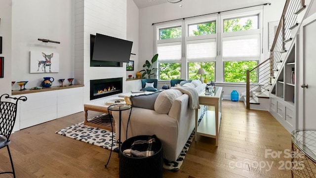 living area featuring stairs, a lit fireplace, and hardwood / wood-style floors
