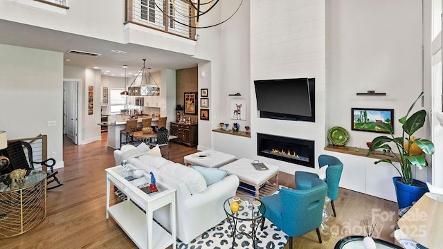 living room with a towering ceiling, visible vents, wood finished floors, and a fireplace