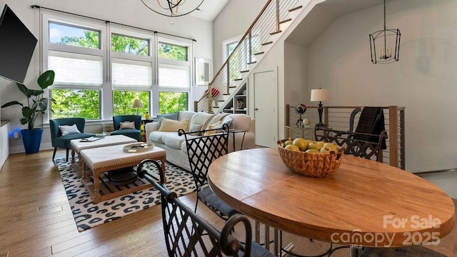 dining room with a high ceiling, a notable chandelier, hardwood / wood-style floors, stairs, and baseboards