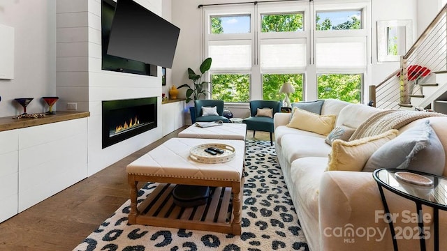 living area featuring stairway, plenty of natural light, a warm lit fireplace, and wood finished floors