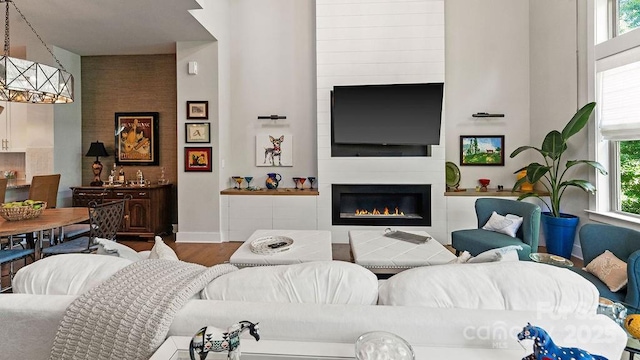 living room with a healthy amount of sunlight, a large fireplace, wood finished floors, and a towering ceiling