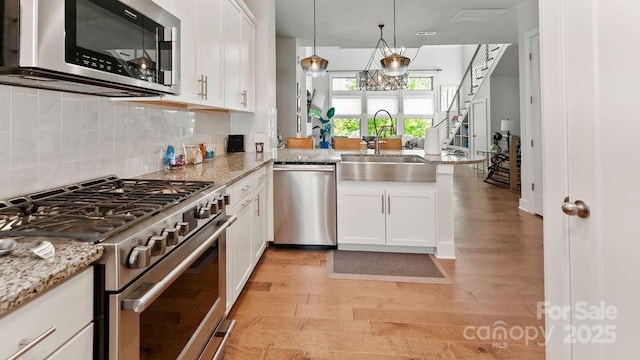 kitchen with stainless steel appliances, a sink, light wood-style flooring, and a peninsula
