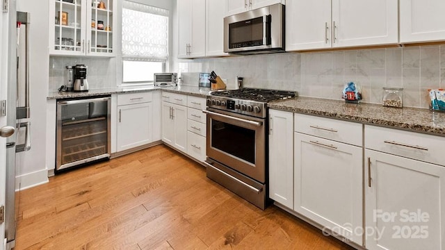 kitchen with white cabinets, appliances with stainless steel finishes, light wood finished floors, wine cooler, and glass insert cabinets