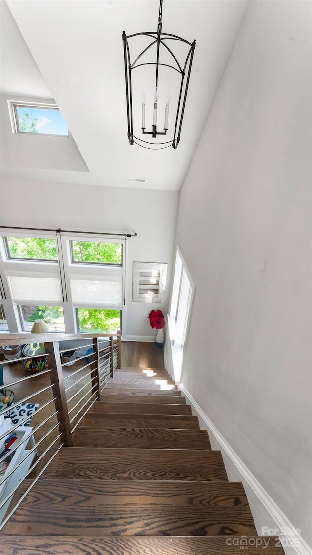 stairs with baseboards, wood finished floors, and a notable chandelier