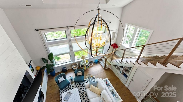 interior space with a high ceiling, a notable chandelier, baseboards, wood finished floors, and visible vents